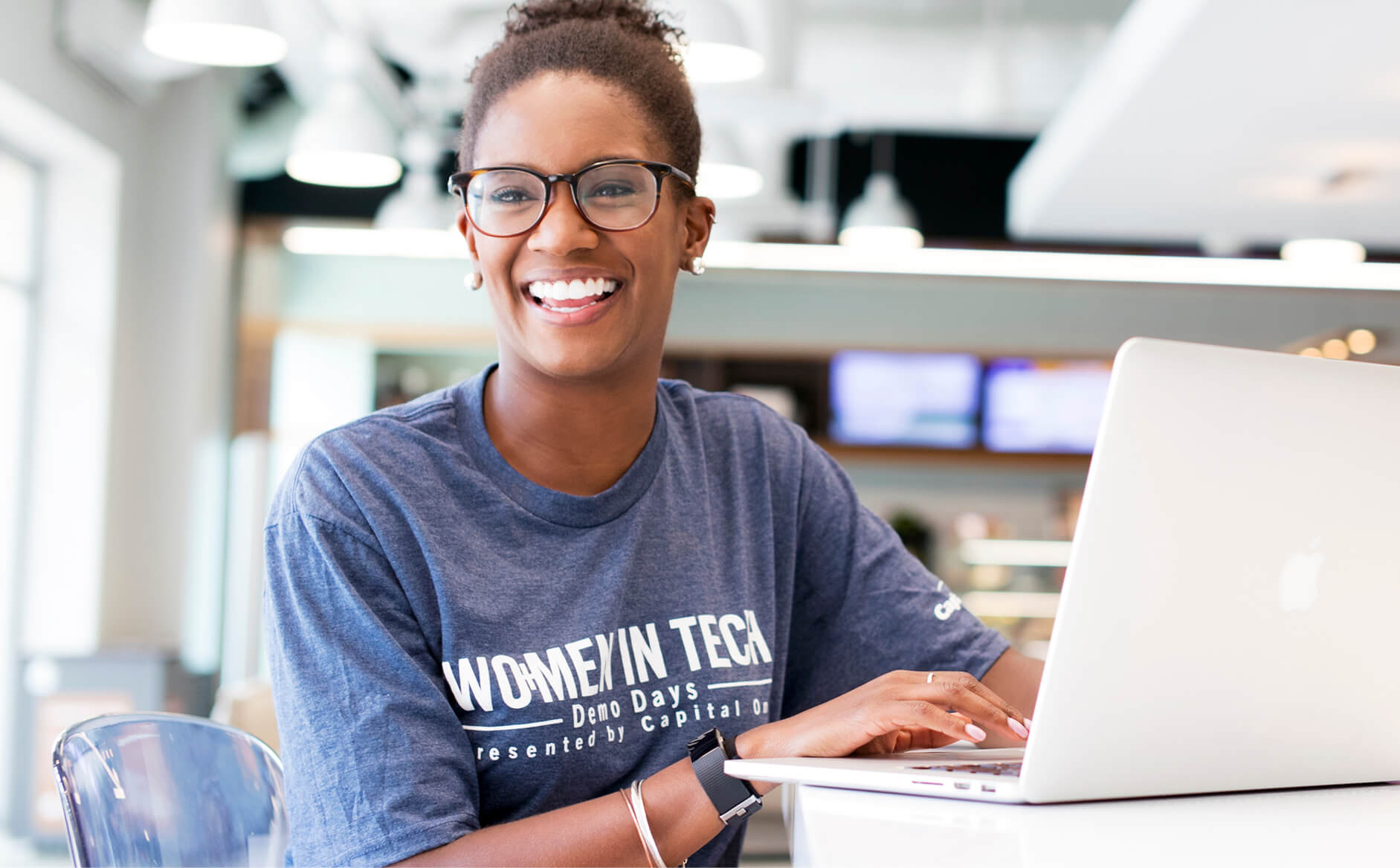 Capital One Tech associate sitting at her laptop and smiling at the camera